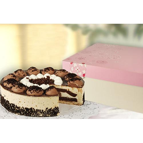 Een ronde laagjescake staat naast een wit-roze PAPSTAR GmbH taartdoos vierkant, 30x30 cm, "Lovely Flowers" (15 stuks), met chocoladestrooisels aan de zijkanten, uitgestald op een kantpatroon oppervlak.