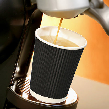 Een Starpak 25 drinkbeker, karton „To Go“ Ripple Wall-beker staat op een metalen lekbak onder de uitloop van een koffiezetapparaat, terwijl hete koffie erin stroomt, en steekt af tegen een zacht verlichte, warm getinte achtergrond.