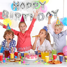 Vier Kinder mit Partyhüten feiern Geburtstag an einem dekorierten Tisch mit Kuchen und Partyartikeln. Dahinter schmückt das Folienluftballon-Set „Happy Birthday“ der PAPSTAR GmbH in Silber und bunte Luftballons die Wand.