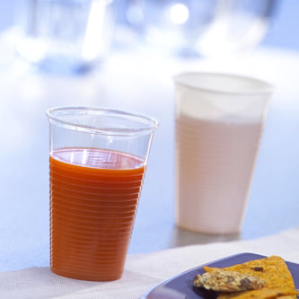 Neben einem mit Orangensaft gefüllten Starpak 25 Trinkbecher (PP, 0,2 l, Ø 7,03 cm × 9,9 cm) steht ein weißer Plastikbecher mit einem leichten Getränk, davor ist ein Teil eines Speisetellers zu sehen – perfekt für den Genuss unterwegs.