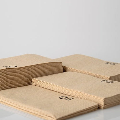 Vier stapels PAPSTAR servetten 3-laags, 33x33 cm, natuur, van gerecycled papier (100 stuks) van PAPSTAR GmbH liggen op een wit oppervlak. Elk gerecycled servet is in de hoek voorzien van een klein zwart recyclingsymbool.