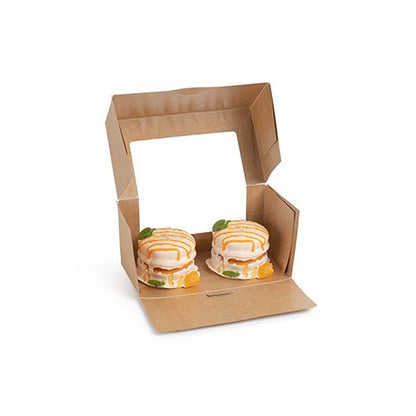 Een PAPSTAR 25 taartdozen met hoekige deksel met PLA-venster van de PAPSTAR GmbH is geopend en toont twee kleine ronde taarten met witte glazuur, oranje spetters en stukjes fruit erin.