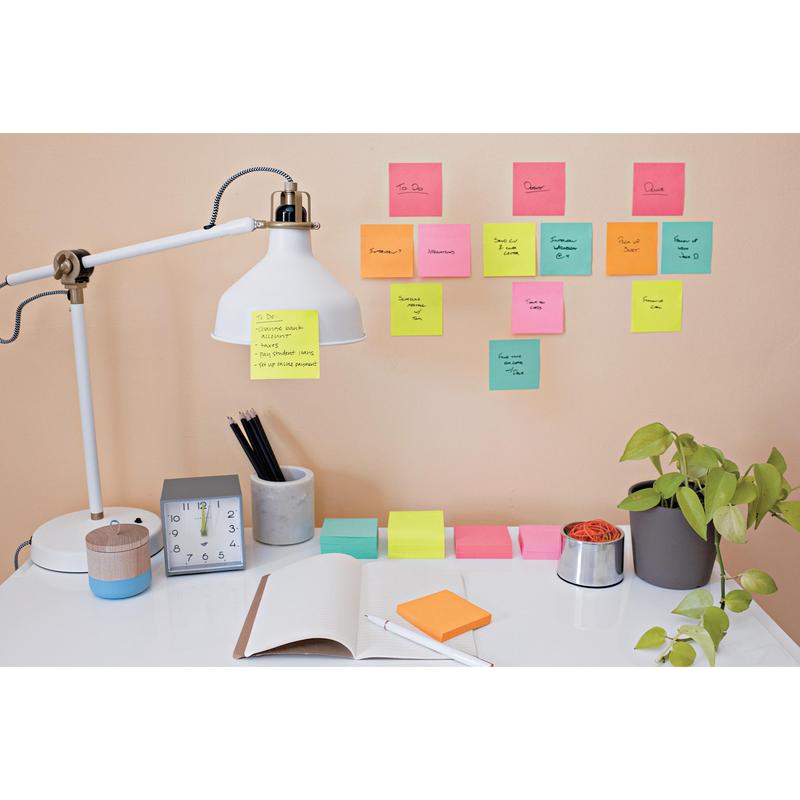 Een opgeruimd bureau met lamp, klok, plant, pennenhouder, een opengeslagen notitieboek en pennen. Aan de muur boven het bureau zijn kleurrijke Post-it® Notes kubus Ultra-kleuren van 3M Nederland B.V. voor handgeschreven herinneringen en taken aangebracht.