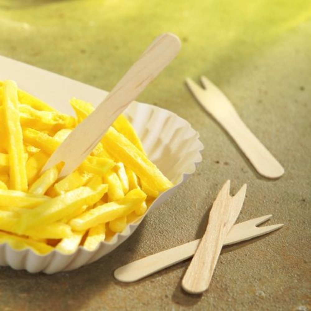 Ein Tablett mit goldbraunen Pommes Frites, auf dem eine PAPSTAR „pure“ Pommes-Frites-Gabeln Holz 8,5 cm liegt, auf einer strukturierten Oberfläche platziert. Zwei weitere PAPSTAR-Holzgabeln liegen daneben. Die Szene wird mit sanftem, natürlichem Licht beleuchtet.