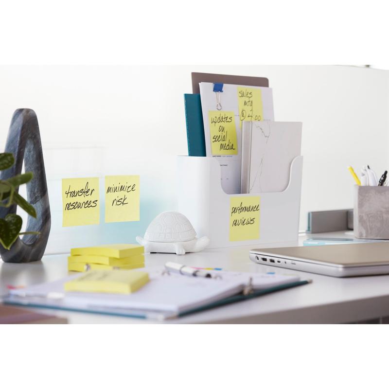 Een opgeruimde bureautafel met Post-it® Super Sticky Notes (76x127 mm, 90 vel, 100% PEFC) van 3M Deutschland GmbH op een glazen scheidingswand, daarbij ordners in een houder, een schildpadfiguur, kantoormateriaal, een gesloten laptop en een open notitieboek met pen.