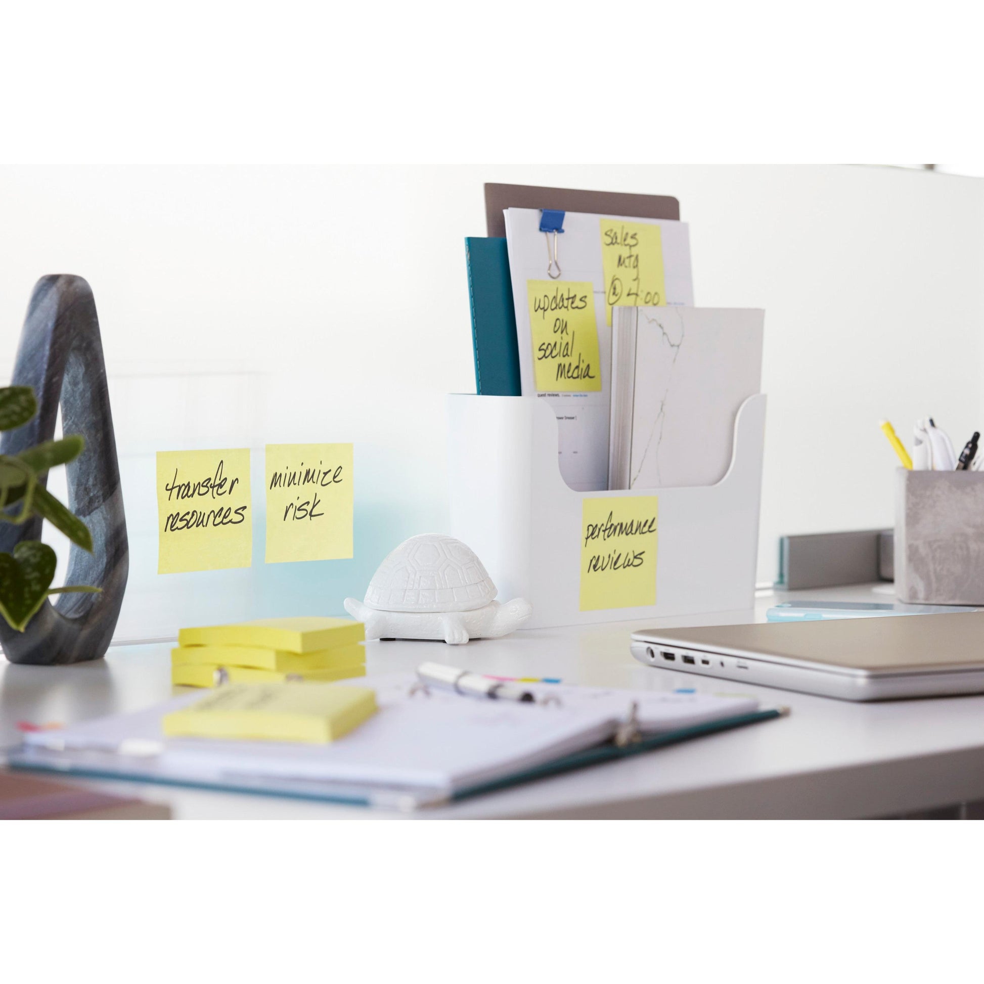 Ein aufgeräumter Bürotisch mit 3M Deutschland GmbH Post-it® Super Sticky Notes (Gelb, 47,6 mm x 47,6 mm), Ordnern in einem weißen Organizer, Notizblöcken, Stiften, einem geschlossenen Laptop, einer Schildkrötenfigur und einer Pflanze. Die Zettel zeigen Erinnerungen und Aufgaben an.