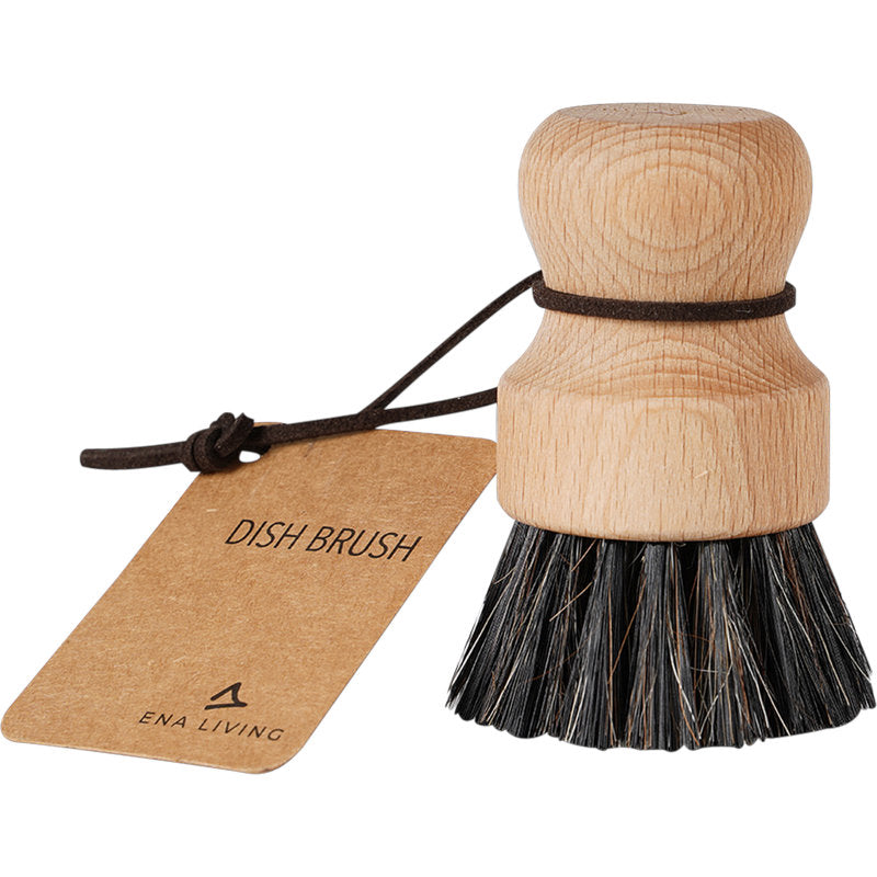 Die ENA Living Topfbürste mit weichen Borsten von Abena Re-Seller GmbH hat einen runden Holzkopf, einen kurzen Stiel, eine Lederschlaufe und ein Schild "DISH BRUSH" - ideal für die sanfte Küchenreinigung. Erhältlich in einem Karton mit 12 Packungen.