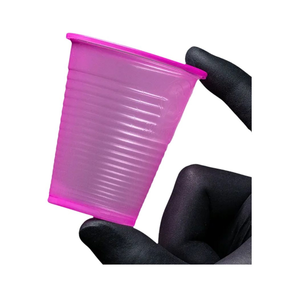 Een kleine, roze AMPri Dental PP mondspoelbeker van polypropyleen wordt tussen twee gehandschoende vingers voor een witte achtergrond gehouden. Deze wegwerp-mondspoelbeker van de AMPri Handelsgesellschaft mbH, die vaak in tandartspraktijken te vinden is, heeft een gestructureerd oppervlak met horizontale groeven.