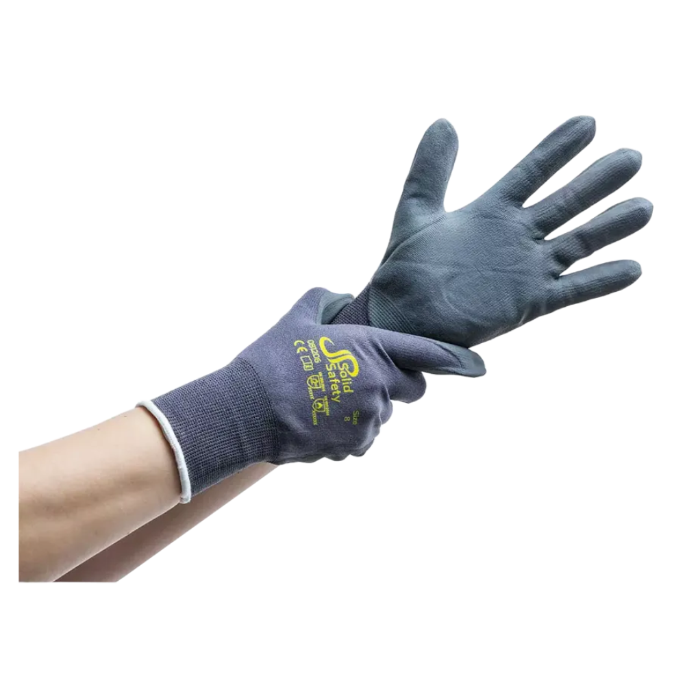 Een persoon draagt aan de rechterhand een donkerblauwe, met rubber beklede handschoen en trekt aan de linkerhand een bijpassende handschoen aan. Deze ultralichte montagehandschoenen AMPri SolidSafety Tough Micro Touch, verkrijgbaar in de maten S tot XXL en geproduceerd door de AMPri Handelsgesellschaft mbH, zijn bedrukt met gele tekst en symbolen op de rug. De achtergrond is eenvoudig wit.