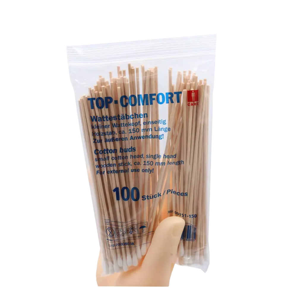 Een hand houdt een doorzichtige plastic verpakking met AMPri TOP-COMFORT wattenstaafjes, perfect voor de ziekenhuisverzorging. De verpakking bevat 100 wegwerp-wattenstaafjes met houten stokjes, productdetails zijn zowel in het Duits als in het Engels vermeld.