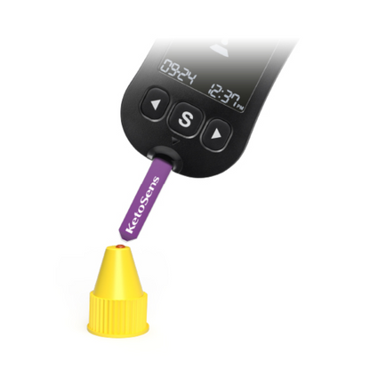 Een digitaal meetapparaat met een display '09:24' en '12:37 uur' wordt gebruikt om een paarse strip met het opschrift 'Alphacheck KetoSens β-Keton-controleoplossing L+M | Verpakking (2 flesjes)' te testen. De strip Alphacheck KetoSens β-Keton-controleoplossing L+M | Verpakking (2 flesjes) wijst naar een kleine gele dop. Het apparaat heeft een grote 'S'-knop onder het display.