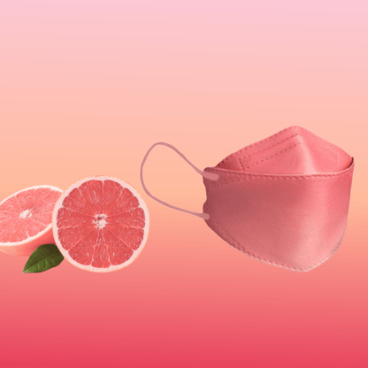 Een deeltjesfilterende Altruan Designer-gezichtsmasker (FFP2-norm) is elegant naast twee halve grapefruits op een roze achtergrond met kleurverloop geplaatst en benadrukt haar stijlvolle ontwerp en ergonomische pasvorm.