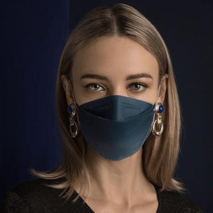 Een persoon met lang haar draagt een Altruan Designer-gezichtsmasker Deeltjesfilterend in blauw, die effectieve bescherming biedt volgens de FFP2-norm. Ze combineert het met grote decoratieve oorbellen voor een donkere achtergrond en draagt een zwart shirt.