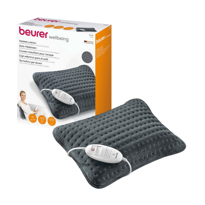 Afbeelding van het Beurer HK 48 Sofa-verwarmingskussen Cosy. Het donkergrijze, gestructureerde verwarmingskussen van Beurer GmbH beschikt over een geïntegreerde besturingseenheid en een geavanceerd veiligheidssysteem. Achter het kussen bevindt zich een doos met productmerken, afbeeldingen en beschrijvingen.
