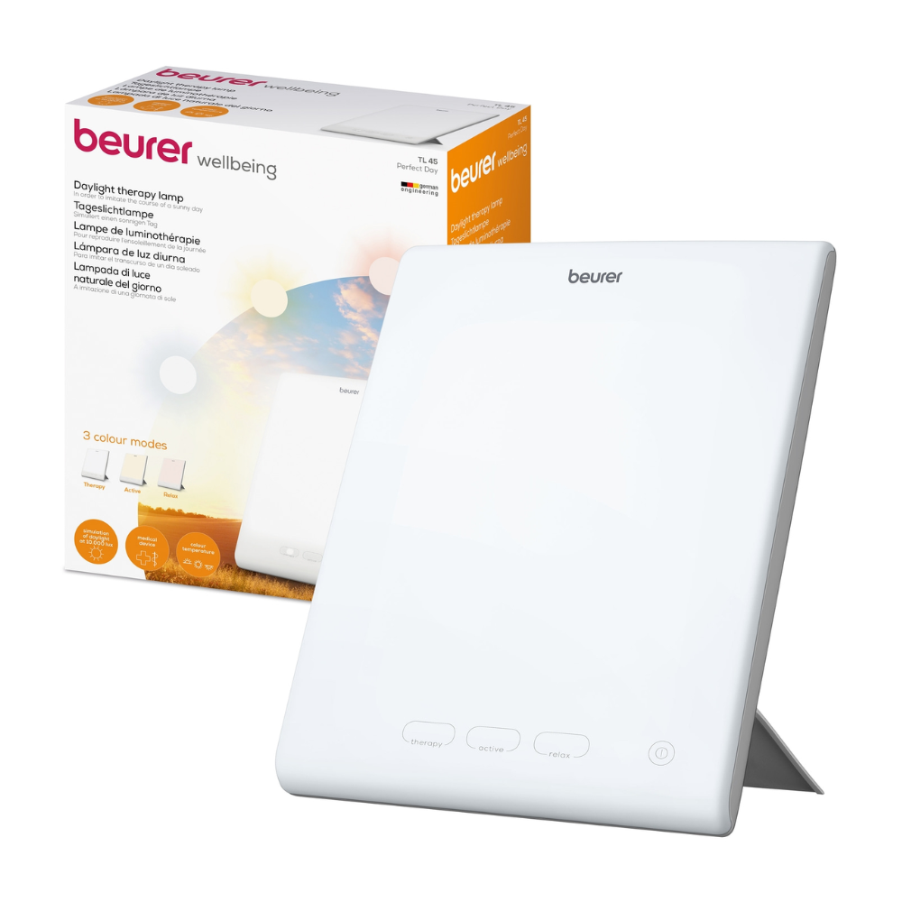 Een witte Beurer Perfect Day daglichtlamp TL 45 van Beurer GmbH wordt naast de verpakking getoond. Op de verpakking zijn de productnaam en de beschrijving in meerdere talen te vinden, waarbij verschillende kleurtemperatuurmodi worden weergegeven. De lamp heeft een eenvoudig ontwerp met knoppen aan de voorkant, waardoor deze ideaal is voor het reguleren van uw dag-nachtritme.