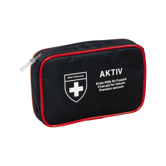 Een compacte zwarte EHBO-set met rode rand en ritssluiting, een wit kruislogo en de teksten „Holthaus Medical AKTIV“ en „Erste-Hilfe für Freizeit / First-aid for Leisure / Premiers secours“ op de voorkant. Perfect voor onderweg en thuis.