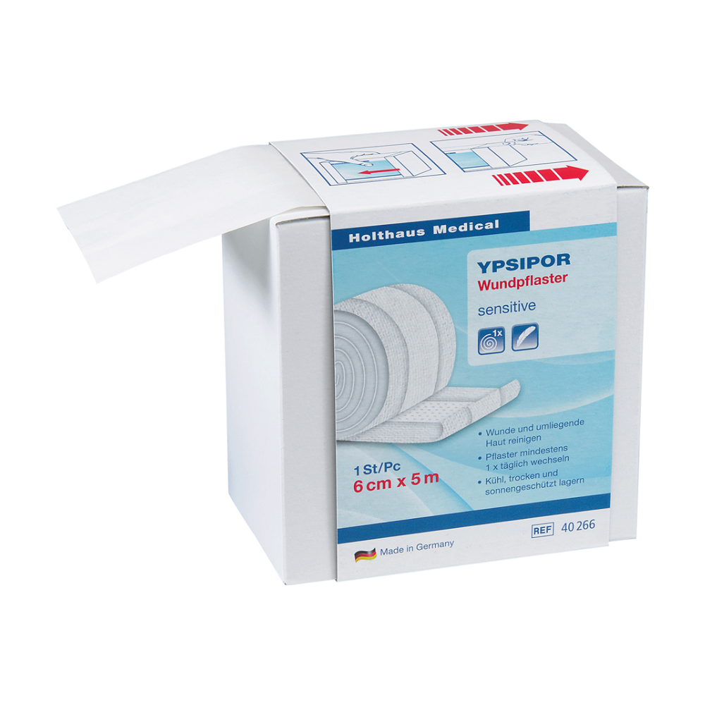 Afgebeeld is een doos Holthaus Ypsipor wondpleisters vlies van Holthaus Medical GmbH & Co. KG. Op de doos staat dat het gevoelig is, 6 cm x 5 m meet en in Duitsland wordt geproduceerd. Een deel van de huidvriendelijke vlies-wondverbandrol is zichtbaar en steekt uit de doos.