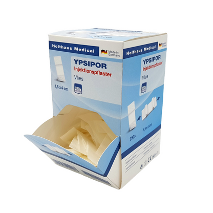 Een rechthoekige doos Holthaus Ypsipor injectiepleisters van Holthaus Medical GmbH & Co. KG met de opdruk 'Made in Germany'. De doos is overwegend lichtblauw en wit, meet 1,5 x 4 cm, bevat 250 vliespleisters met absorberend kussen en is afgebeeld met een geopende bovenklep die de inhoud vrijgeeft.