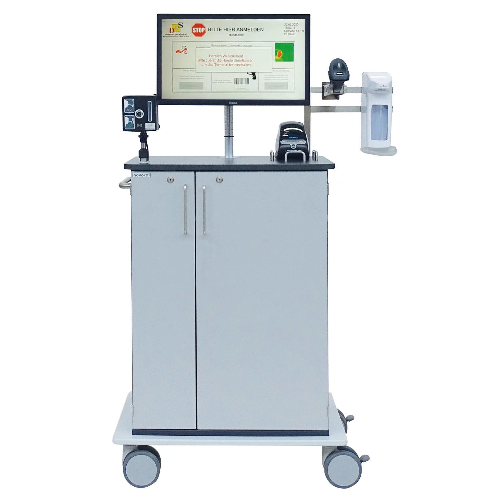 Der Novocal Digitaler Empfangsassistent mit Temperaturmessung ist ein mobiler Medizin-Workstationwagen mit Monitor, Barcode-Scanner, Handdesinfektionsspender, Drucker sowie Besucherregistrierung und zwei Schranktüren auf vier Rollen.