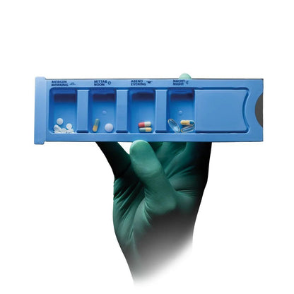 Een gehandschoende hand houdt een blauwe Med-Comfort PP wegwerp medicijndispenser (4 vakken, 22,2 x 6 x 1,5 cm) van AMPri Handelsgesellschaft mbH, elk gelabeld vak is gevuld met tabletten; de achtergrond is wit.