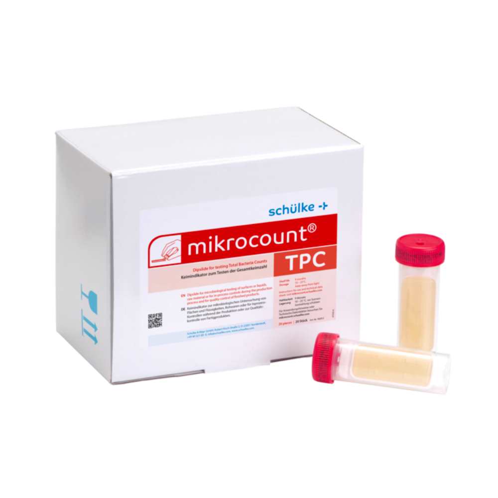 Een witte doos met het opschrift „Schülke & Mayr GmbH Mikrocount® TPC, voedingsbodem | Verpakking (20 stuks)“ met een logo en een productbeschrijving naast twee flesjes voor microbiële tests, één met een gele dop, de andere met een doorzichtige dop.