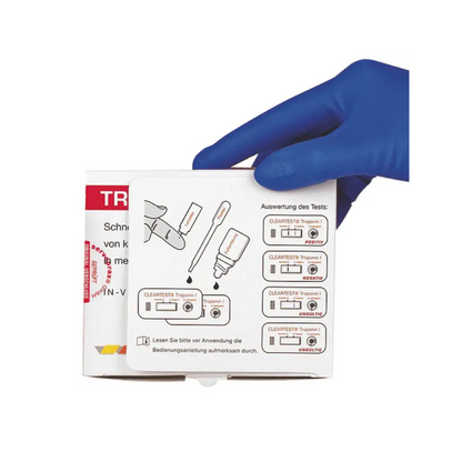 Een hand met een blauwe handschoen houdt een doos met instructies voor de Cleartest® Troponin I Volbloed Infarct-test van Servoprax GmbH, die van cruciaal belang is voor de diagnose van een hartinfarct. De gedetailleerde afbeeldingen geven aanwijzingen voor het gebruik van een pipet en voor de interpretatie van de als positief en negatief gemarkeerde resultaten met tekst in het Duits.