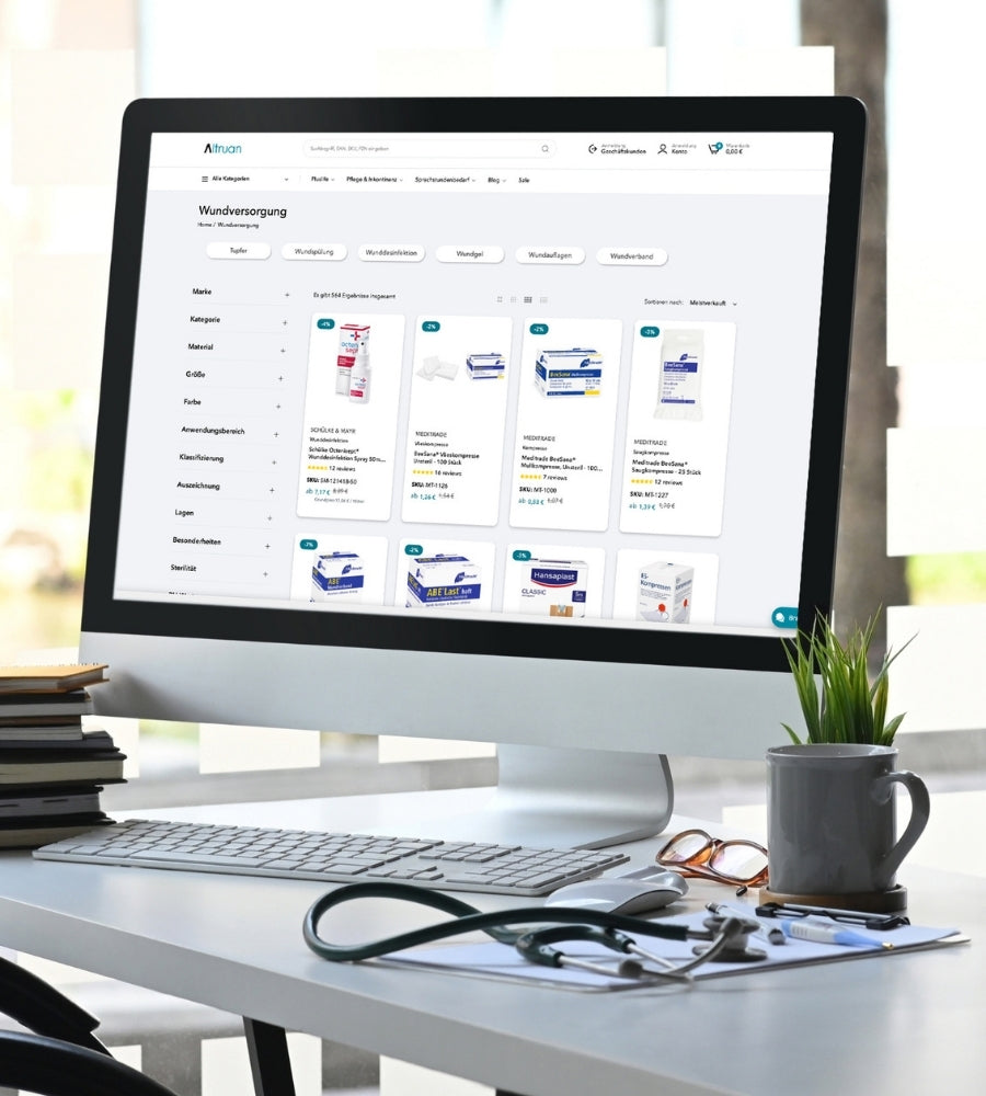 Auf einem Computermonitor wird eine Website für medizinischen Bedarf angezeigt, auf der Produkte zur Wundversorgung vorgestellt werden. Auf dem Schreibtisch neben dem Monitor liegen ein Stapel Notizbücher, ein Stethoskop und eine Topfpflanze.