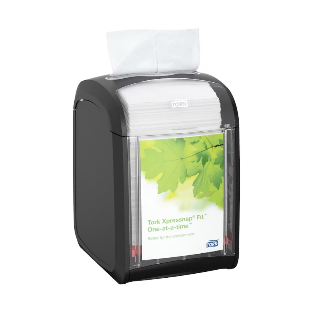 Der Tork Xpressnap Fit® 272900 Tischspender für Servietten von TORK – Essity Professional Hygiene Germany GmbH hält elegant weiße Servietten. Auf dem mit grünen Blättern verzierten Frontetikett steht stolz „Tork Xpressnap Fit One-at-a-time“ und betont damit den reduzierten Serviettenverbrauch und das Engagement für die Umwelt.