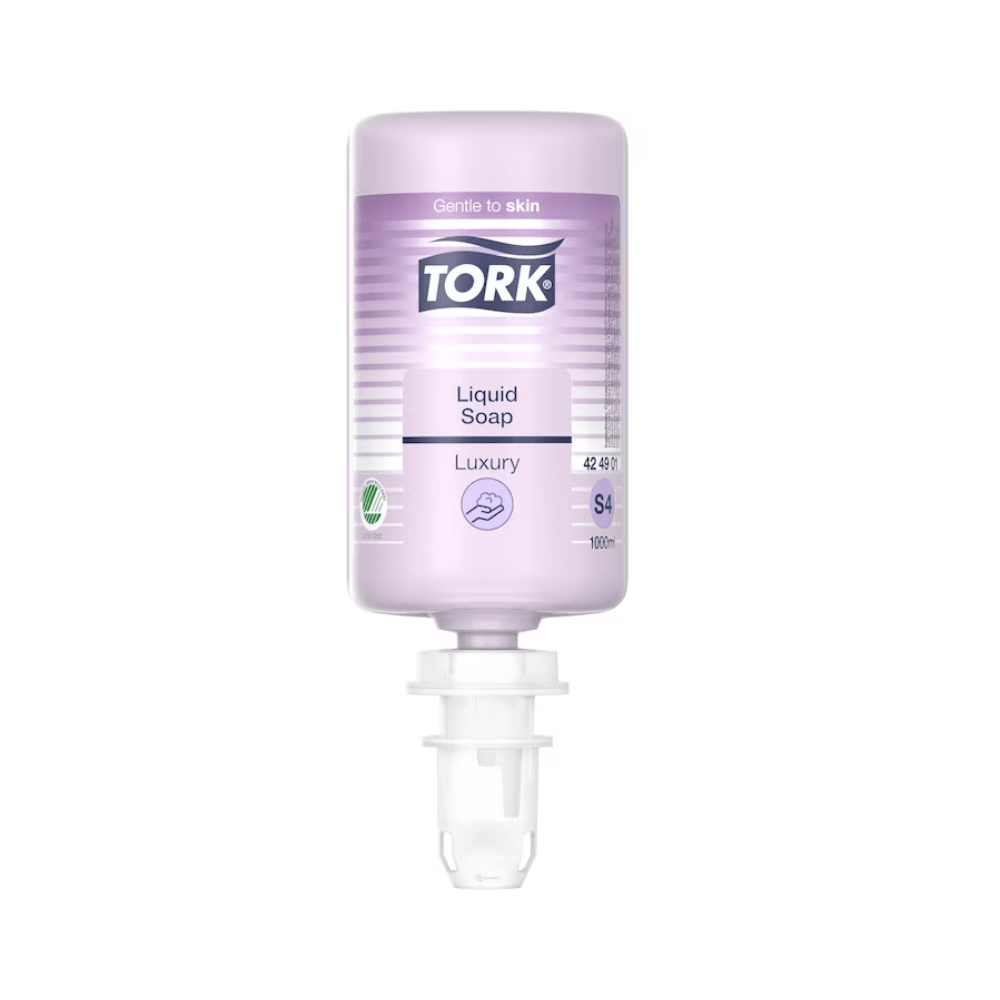 Een heldere fles Tork luxueuze vloeibare zeep van Essity Professional Hygiene Germany GmbH, gemarkeerd als 'Luxe' en 'Zacht voor de huid', verrijkt met magnolia-extract. De zeep is paars en behoort tot het S4-systeem, heeft een doseertuit aan de onderkant en biedt een volume van 1000 ml.
