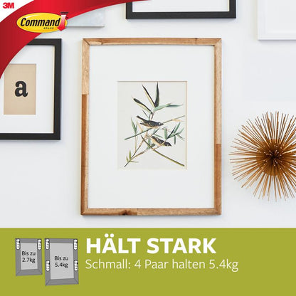 Een ingelijste plantenprint hangt aan een witte muur met andere lijsten en een goudobject. Onderaan worden de Smalle Command™ Bevestigingsstrips voor schilderijen (M) 17207 van 3M Deutschland GmbH geprezen om hun residuvrije en sterke houdkracht.