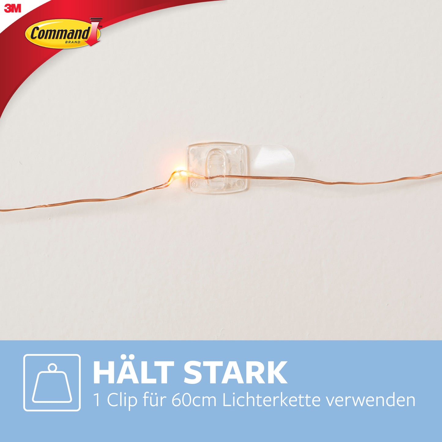 Een Command™ decoratieclip, transparant met transparante strips van 3M Deutschland GmbH, houdt een lichtsnoer aan de muur. Op de afbeelding is een blauwe doos met Duitse tekst en Command-logo linksboven te zien.