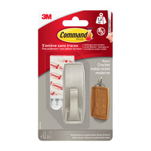 Eine Packung Command™ Metallhaken "Modern Reflection" der 3M Deutschland GmbH enthält einen Nickelhaken, zwei Klebestreifen, eine Montageanleitung und ein Beispielbild, auf dem der Haken einen Holzgegenstand hält.