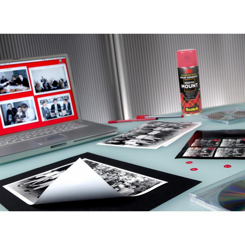 Een werkgebied met een laptop met fotobewerkingssoftware, zwart-wit afdrukken, een blik 3M™ Scotch® PhotoMount™ lijmspray (400 ml, 1 blik, 3M Deutschland GmbH), een leeg vel voor montage, een doorzichtige cd-hoes en rode kleefpunten op een glazen tafel.