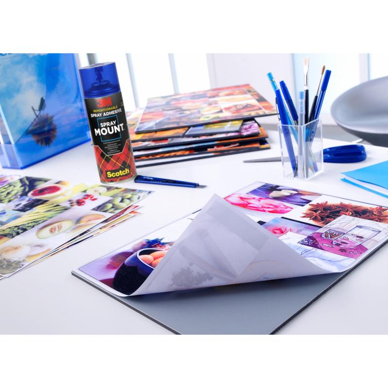 Een creatieve werkplek bij het heldere raam met glanzende foto's, penselen, pennen, scharen, mappen en het 3M™ Scotch® SprayMount™ lijmspray (400 ml, 1 blik/verpakking) van 3M Deutschland GmbH - ideaal voor fotocollages en knutselwerk.