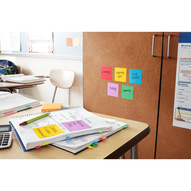 Een klaslokaal met geopende schriften, een rekenmachine en papieren op een bureau. 3M Post-it® Super Sticky Z-Notes (Boost Collection, 76x76mm, PEFC) labelen schoolvakken op een kast. Lege stoelen en posters vullen de achtergrond.