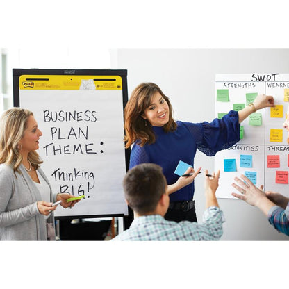 Een vrouw wijst met gebaren naar een SWOT-analyse op een whiteboard, terwijl haar collega's toekijken. Een ander staat naast een flipchart met de tekst "Business Plan Theme: Thinking Big!" Allen gebruiken 3M Post-it® Notes (76x76 mm, geel, 6 blokken/verpakking).