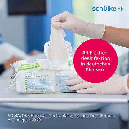 Een persoon met witte medische handschoenen trekt een Schülke Mikrozid® universal wipes desinfectiedoekje premium uit een houder op een tafel. De tekst op de afbeelding bevat '#1 Oppervlaktedesinfectie in Duitse klinieken' en informatie over IQVIA en het DKB-ziekenhuis in Duitsland.